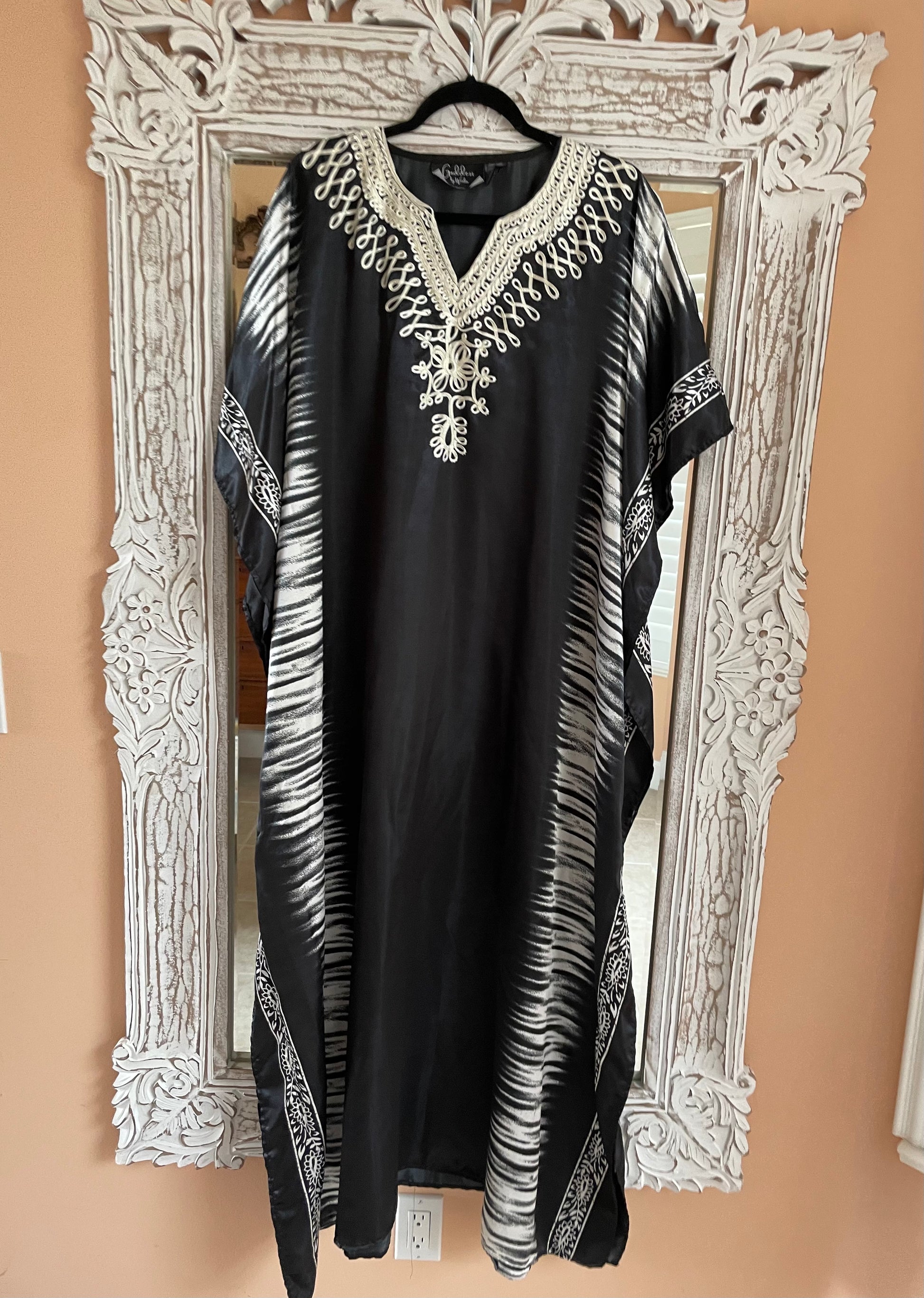 Black dress with white embroidery on a hanger in front of an ornate mirror.