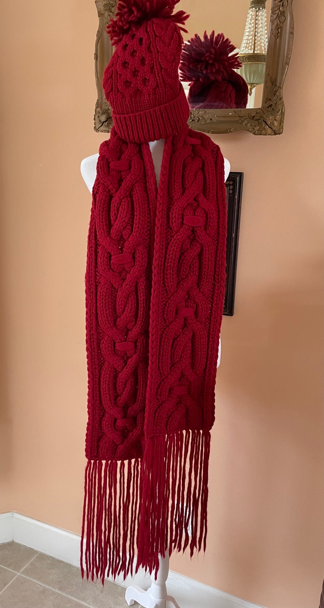 Red knitted scarf with fringe on a mannequin against a beige wall.